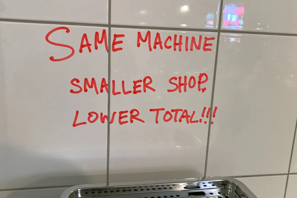 Red marker on kitchen tiles: "Same machine, smaller shop, lower total!!"