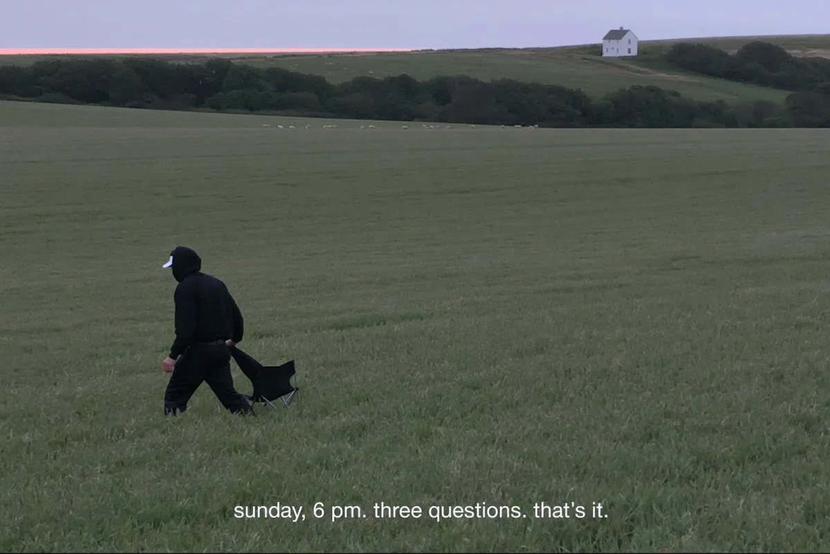Person setting up a chair in a field at dusk: "sunday, 6 pm. three questions. that's it."